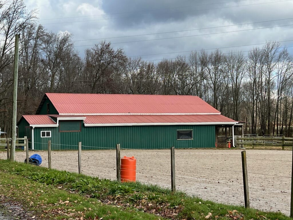 Custom Pole Barn Construction In Strasburg, Pa 4 Custom Pole Barn Construction In Strasburg, Pa With Green Metal Siding, Red Metal Roof, And Spacious Post-Frame Design For Agricultural And Equestrian Use.