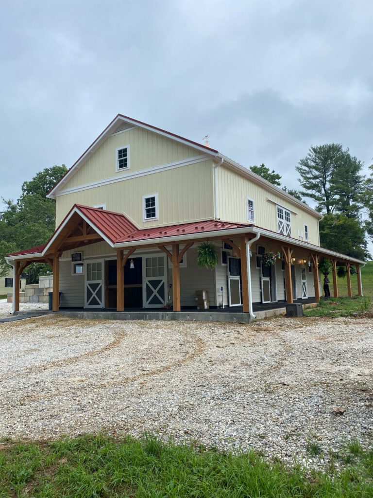 Custom Pole Barn In Lititz, Pa With Wraparound Covered Porch, Exposed Timber Posts, Barn-Style Doors, And Red Metal Roofing.